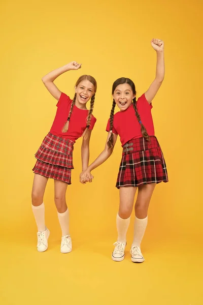 Está na hora de relaxar. meninas de moda vermelha. moda estilo inglês. meninas felizes em saia quadriculada. olhar de beleza. crianças felizes no fundo amarelo. felicidade infantil. uniforme da escola na moda. salto engraçado — Fotografia de Stock