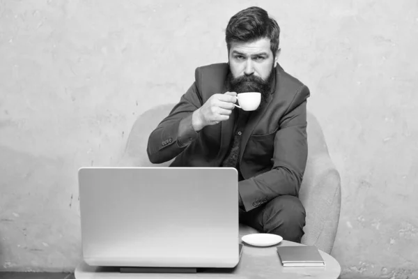 Im mobilen Stil. bärtiger Mann genießt sein Heißgetränk und sein mobiles Internet. Geschäftsmann mit mobilen Geräten, die am Arbeitsplatz Tee oder Kaffee trinken. Hipster in Formalbekleidung am Laptop im mobilen Büro — Stockfoto