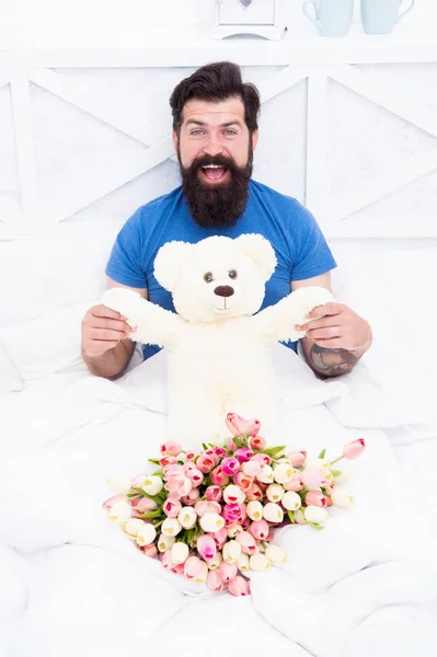 Express positivity. cheerful bearded man in bed. birthday gift. spring fresh tulip and bear toy. love valentines day. womens day. flowers for march 8. good morning surprise. happiness about present