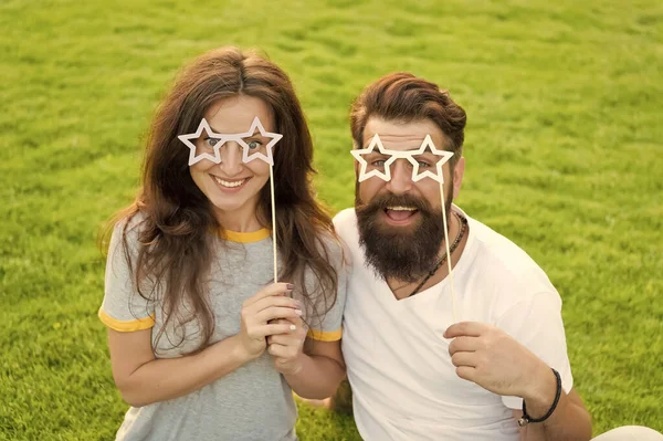 Bons adereços. Casal engraçado segurando adereços de fotocabine em forma de estrela em paus. Família feliz comemorando com adereços de festa. Homem barbudo e mulher sensual sorrindo com adereços extravagantes na grama verde — Fotografia de Stock