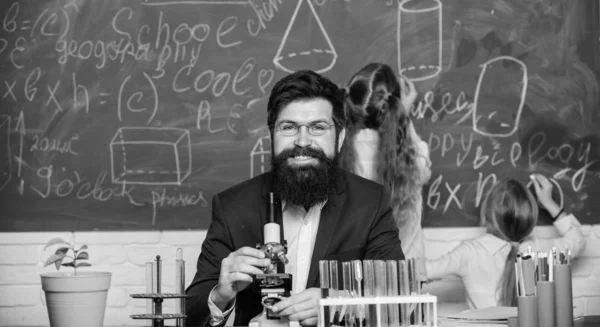 Biology plays role in understanding of complex forms of life. School teacher of biology. Man bearded teacher work with microscope and test tubes in biology classroom. Explaining biology to children