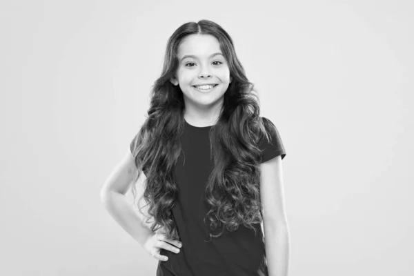 Uma menina a sorrir. menina feliz com cabelo encaracolado longo. moda e beleza. Criança hipster. felicidade infantil. salão de cabeleireiro. cuidados com a pele e cabelo natural. beleza natural. pequena beleza sorrindo — Fotografia de Stock