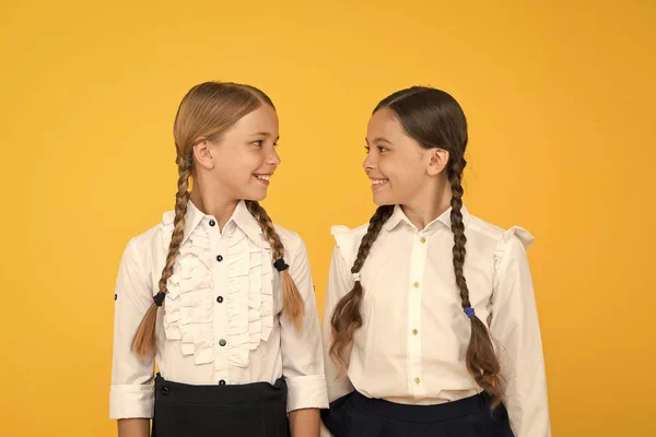 我们喜欢学习。快乐的孩子穿制服。黄色背景的小女孩。友谊和姐妹情谊。最好的朋友。孩子正式时尚。国外教育。聪明的孩子。学校朋友 — 图库照片