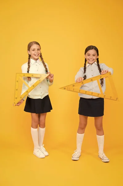 Los niños lindos estudiantes estudian matemáticas. Día del conocimiento. Pasar de la teoría a la práctica. Excelentes alumnos. Secundaria. Colegialas apariencia ordenada uniforme escolar celebrar grandes reglas para la lección de la escuela de geometría —  Fotos de Stock