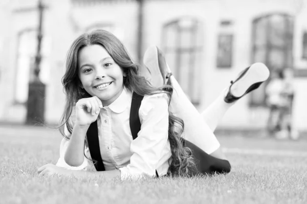 Pequeña colegiala. Relájate en el patio del colegio. Buen momento. Vacaciones escolares para descansar. Adorable alumno. Niña yaciendo hierba verde. Niño relajándose al aire libre. Chica uniforme escolar disfrutar de relajarse. Cuídate. — Foto de Stock