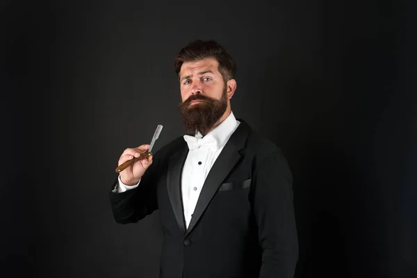 Echte stijl voor een echte man. Een man met een baard houdt een scheermes vast. Professionele man met lange snor en baard haar. Brutale man in smoking pak. Hipster met formele uitstraling. Kapperszaak. November voor gezichtshaar — Stockfoto