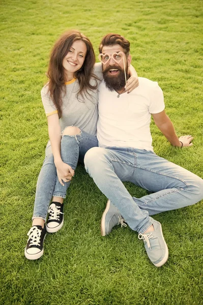 Man bearded hipster and pretty woman in love. Summer vacation. Emotional couple radiating happiness. Love story. Couple relaxing green lawn. Happy together. Couple in love cheerful youth booth props