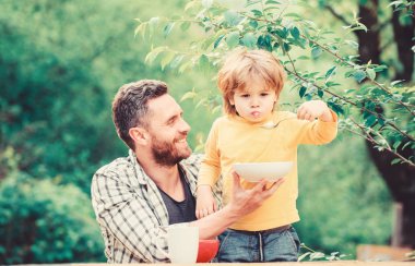 Yaz kahvaltısı. Sağlıklı gıda kavramı. Bebeği besliyor. Çocuklar için menü. Aile ev yapımı yemeklerin tadını çıkarır. Baba oğul yemek yer ve eğlenir. Yemek alışkanlıkları. Baba gıda doğa arka plan yeme ile küçük çocuk
