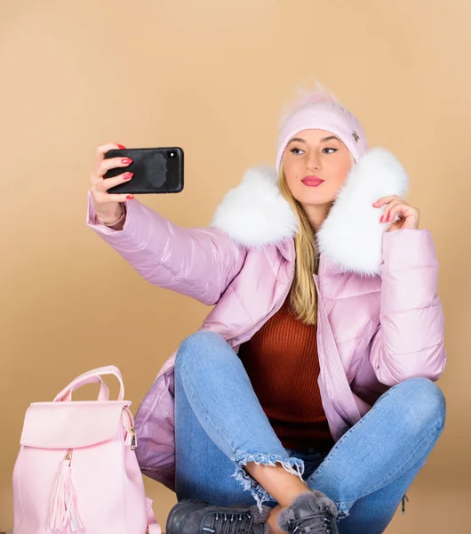 Děvče v nafouklém kabátě dělá selfie. Faux kožešinová móda. teplé zimní oblečení. Zavolej Selfiemu. chřipka a studené období. Kožená taška. žena v čepici s batohem. Veselé zimní prázdniny. webový blogger — Stock fotografie