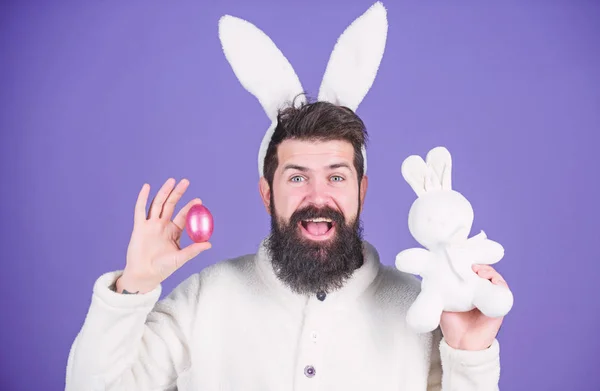 Весна, нове життя і родючість. Щасливий чоловік з кролячими вухами тримає іграшку та яйце. Бородатий чоловік у костюмі кролика з пасхальним яйцем та іграшкою заєць. Святкування весняних свят. Радісно про Великдень — стокове фото