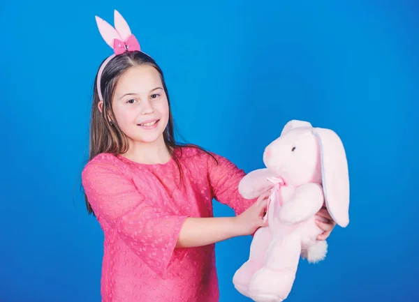 快乐的童年。兔子耳朵配件。可爱的顽皮的兔子孩子拥抱软玩具。兔子女孩与可爱的玩具在蓝色背景。孩子微笑玩兔子玩具。祝复活节幸福。获得复活节精神 — 图库照片