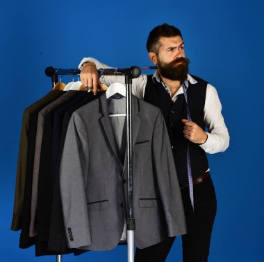 Yelekli sakallı adam elbise rafında. Moda seçimi