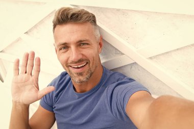 Merhabalar. Adam fotoğraf çeken akıllı telefondan el sallıyor. Çevrimiçi video yayınlanıyor. Gezici internet. Blog için çekim. Olgun bir blogcu. İnternet günlüğü içeriği. Kişisel blog konsepti. Günaydın.
