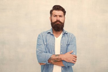 Erkeklik ve erkek güzellik konsepti. Sakallı ve bıyıklı hipster denim gömlek giyer. Bakımlı maço. Gri duvar arka plan üzerinde Acımasız yakışıklı hipster adam. Sakallı adam trendy hipster tarzı