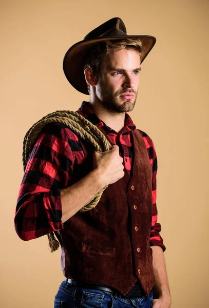 Homem de chapéu segura corda. Ocupações no rancho. Ferramenta de laço de cowboy americano. Lasso é usado em rodeos parte eventos competitivos. O laço pode ser amarrado ou embrulhado. A vida ocidental. Homem cowboy bege fundo — Fotografia de Stock