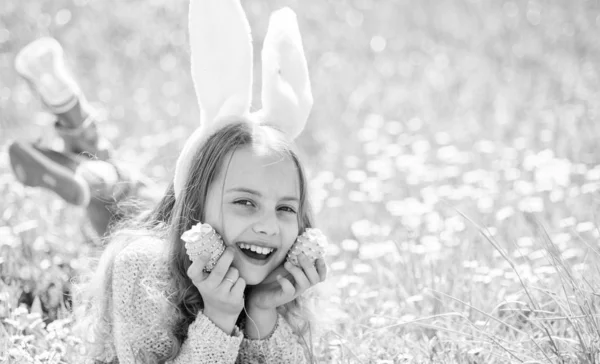 Mädchen mit glücklichem Gesicht hält Ostereier in den Händen, Gras im Hintergrund. Kind mit Hasenohren auf der Wiese liegend, Platz kopieren. Mädchen mit langen Haaren, die an einem sonnigen Frühlingstag auf dem Rasen liegen. Osterkonzept. — Stockfoto