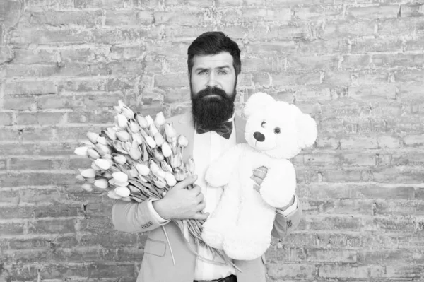 Surprise will melt her heart. Romantic man with flowers and teddy bear. Romantic gift. Macho getting ready romantic date. Man wear blue tuxedo bow tie hold flowers bouquet. International womens day — Stock Photo, Image
