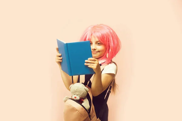 Chica con mochila y juguete lee libro. Niño con sonrisa — Foto de Stock