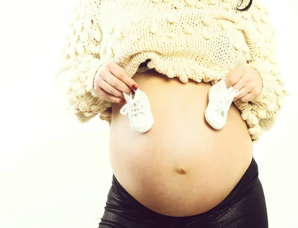 Mãos femininas de mulher grávida segurando botas de bebê na barriga — Fotografia de Stock