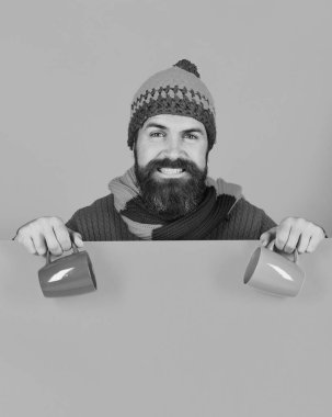 Sıcak şapkalı adam turuncu arka planda beyaz bardak tutuyor.