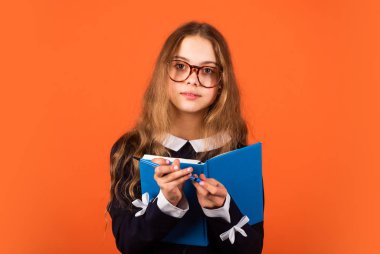 Her zaman güzel ve zeki. Akıllı kız kitabı ve kalem kahverengi arka planı tutuyor. Gözlüklü, zeki görünümlü küçük bir çocuk. Okul ve eğitim. Özel ders. Zeki ve zeki.