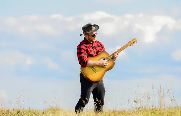 Toca una hermosa melodía. Concepto de música country. Guitarrista cantante country de pie en el fondo del cielo de campo. Músico country inspirado. Canción de senderismo. Hombre guapo con guitarra. Estilo country. Vacaciones de verano — Foto de Stock