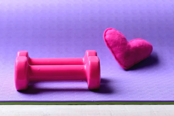 Halteres feitos de plástico rosa perto do coração na textura roxa — Fotografia de Stock
