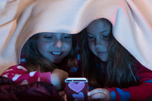 Chica amigos bajo manta jugando con el teléfono móvil — Foto de Stock