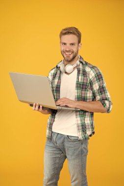 Hipster neşeli sakallı surat dizüstü bilgisayar tutuyor. Laptop tamircisi ya da teknoloji işçisi. İş ve eğlence için not defteri. Adam modern teknolojilerden hoşlanıyor. Kablosuz kulaklıklı dizüstü bilgisayar kullan