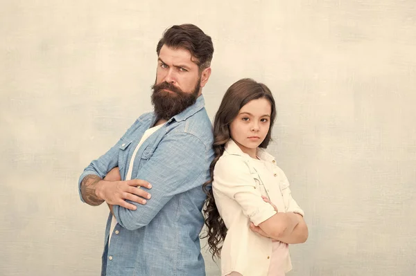 La hija necesita su amor incondicional. Hija pequeña y hombre barbudo con mirada seria. Linda hija y padre manteniendo los brazos cruzados sobre fondo gris. Tratando a su hija con amor —  Fotos de Stock