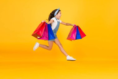 Moda ve markalar. İndirimlere doğru. Alışveriş torbalarıyla atlayan mutlu kız. Kağıt torbalarla gülümseyen küçük bir çocuk. Tatil hazırlıkları ve kutlamalar. Kara Cuma 'da alışveriş. İlham verici alışveriş.