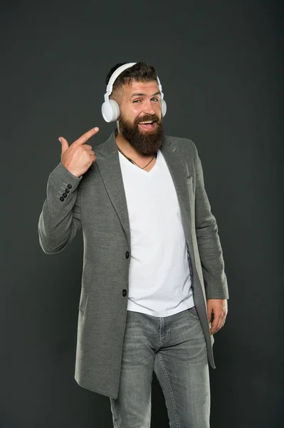 Kijk naar mijn headset. Hipster wijzer vinger naar headset grijze achtergrond. Baard man luisteren naar muziek afspelen in stereo headset. Met behulp van draadloze bluetooth headset voor zaken en plezier. Het moderne leven — Stockfoto