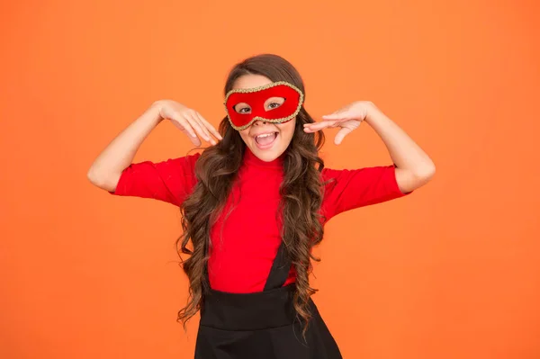 Cambia il tuo look. Bambino felice con partito sguardo sfondo arancione. Vogue sguardo di piccolo modello di moda. La ragazzina indossa una maschera di carnevale. Bellezza. Accessorio di moda festivo. Festa delle vacanze — Foto Stock