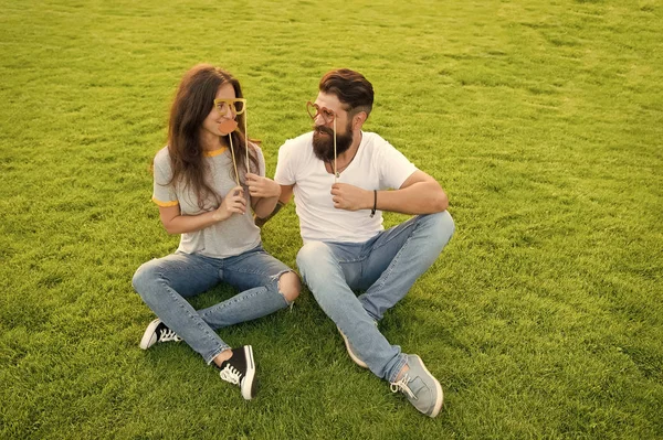 The couple that is meant to be. Couple in love having fun on green grass. Couple of bearded man and sexy woman holding party props on sticks. Family couple relaxing together on summer day