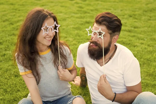 Disfrutando de la cabina de fotos graciosa. Pareja divertida mirando a través de gafas de utilería en hierba verde. Hombre barbudo y mujer sexy haciendo mueca divertida en el día de verano. Divertido y juguetón —  Fotos de Stock