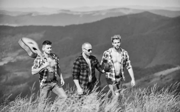 Grupp ungdomar i rutiga skjortor som går tillsammans på toppen av berget. Män med gitarr vandring på solig dag. Turister vandring koncept. Vandra med vänner. Lång rutt. Att njuta av friheten tillsammans — Stockfoto