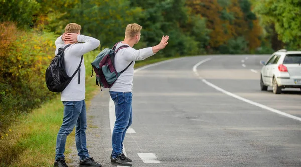 fun of traveling. Enjoying summer hike. Looking for transport. twins walk along road. stop car with thumb up gesture. hitchhiking and stopping car with thumbs up gesture at countryside. On the road