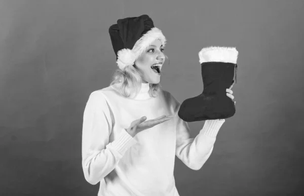 Femme en santa chapeau tenir cadeau de Noël fond rouge. Concept de bas de Noël. Fille visage joyeux obtenu cadeau en chaussette de Noël. Vacances d'hiver traditionnelles. Vérifier le contenu du bas de Noël — Photo