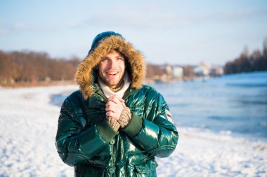 Sıcak ceketli, karlı bir arka plan. Rüzgara dayanıklı kıyafetler. Kışın elverişli hava koşulları. Güneşli kış günü. Kış erkek giyim. Kış kıyafeti. Hipster moda kıyafeti. Kapüşonlu adam.