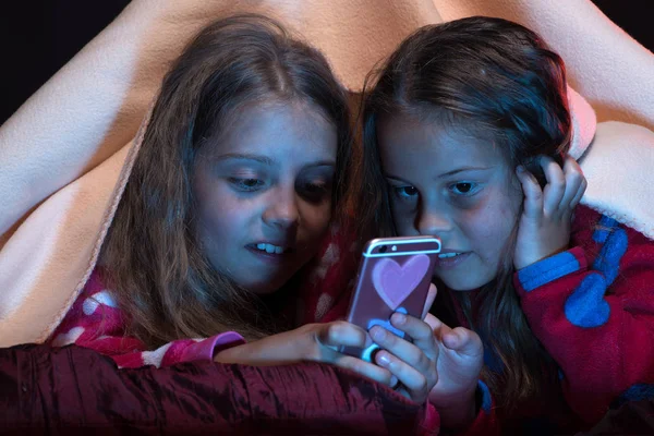 Eerste liefde en vriendschap concept: meisjes onder deken met telefoon — Stockfoto