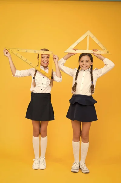 Mentes brillantes. Niños con uniforme en la pared amarilla. amistad y hermandad. niñas pequeñas y felices estudiar matemáticas. estudiantes usan gon ruler. disciplinas del tallo. de vuelta a la escuela. Matemáticas y geometría —  Fotos de Stock