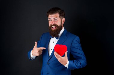 Aşkı kutla. Bana güvenin. Sevgililer günün kutlu olsun. Smokinli adam kırmızı kalbi tutar. Aşk konsepti. Resmi takım elbiseli, tutkulu, olgun aşık hipster. Papyonlu bir iş adamı. Romantik selamlaşma. Aşık ol.