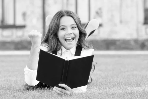 Studuji koncept. Školačka školní uniforma ležící na trávníku s oblíbenou knihou. Mimoškolní čtení. Roztomilé malé dítě čtení knihy venku. Základní vzdělání. Roztomilá holčička se učí číst — Stock fotografie