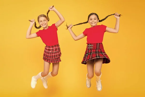Присоединяйся. Весёлые друзья школьницы прыгают на жёлтом фоне. Праздновать праздник. Шотландский праздник. Дети носят клетчатые платья. Национальный праздник. Школьная форма. Шотландский стиль — стоковое фото