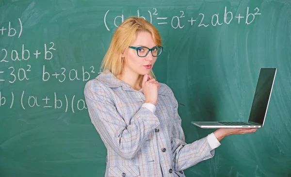 Woman teacher wear eyeglasses holds laptop surfing internet. Basic school education. Digital technologies concept. Educator smart lady with modern laptop surfing internet chalkboard background