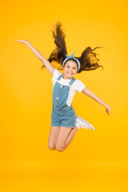 İçinde enerji var. Küçük kız sarı arka plandan atladı. Özgürlüğün tadını çıkar. Çocuk günü konsepti. Özgürlüğün ruhu. Aktif kız özgürlüğü hisseder. Özgür hissediyorum. Kaygısız çocuk. Yaz tatili. Mutluluk atlayışı