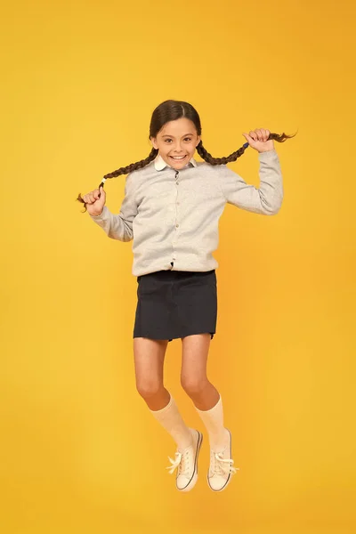 O hiper. Mutlu enerjik çocuk sarı arka plan üzerinde atlama. Uzun saçlı küçük kız enerjik hissediyor. Küçük okul çocuğu okul yılına enerjik bir başlangıç yapıyor. Aktif ve enerjik — Stok fotoğraf