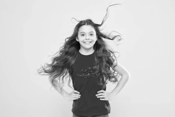 Интересуется моими волосами и моим парикмахером. Happy little girl child smiling with flowing long brunette hair on yellow background. Детский парикмахер. Парикмахерская — стоковое фото