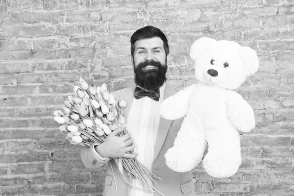 Macho getting ready romantic date. Man wear blue tuxedo bow tie hold flowers bouquet. International womens day. Surprise will melt her heart. Romantic man with flowers and teddy bear. Romantic gift