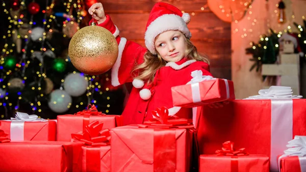 Дитяча щаслива збуджена дівчина знаходить подарунки біля ялинки. Веселого Різдва. Дитячий одяг Санта-капелюх тримає загорнуту різдвяну подарункову коробку. Санта приніс мені подарунки. Щастя і радість. Концепція щасливого дитинства — стокове фото